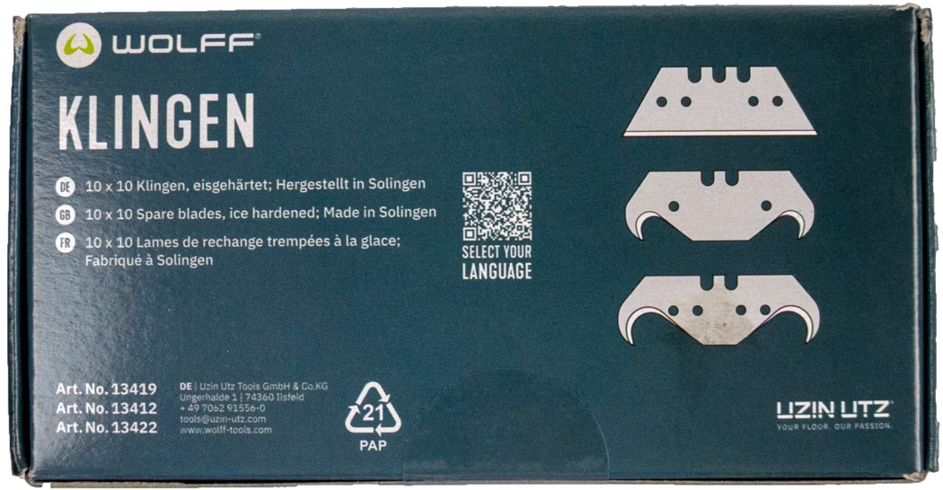 WOLFF_Dummy_13419_13421_blade box_2025-08 Close-up photograph of a rectangular cardboard box of Wolff replacement blades for floor tools. The dark teal packaging displays the brand logo 'WOLFF' at the top left and the large white word 'KLINGEN' on the left side. Three stylized blade illustrations are printed on the right; a small QR code with the caption 'SELECT YOUR LANGUAGE' sits between text blocks. Multilingual product lines name '10 x 10 spare blades, ice hardened; Made in Solingen' in German, English and French. Bottom-left shows three article numbers and manufacturer contact details, and a '21 PAP' recycling symbol appears near the lower centre. The box edges show slight wear and handling marks. Overall a clean product package photographed on a white background.